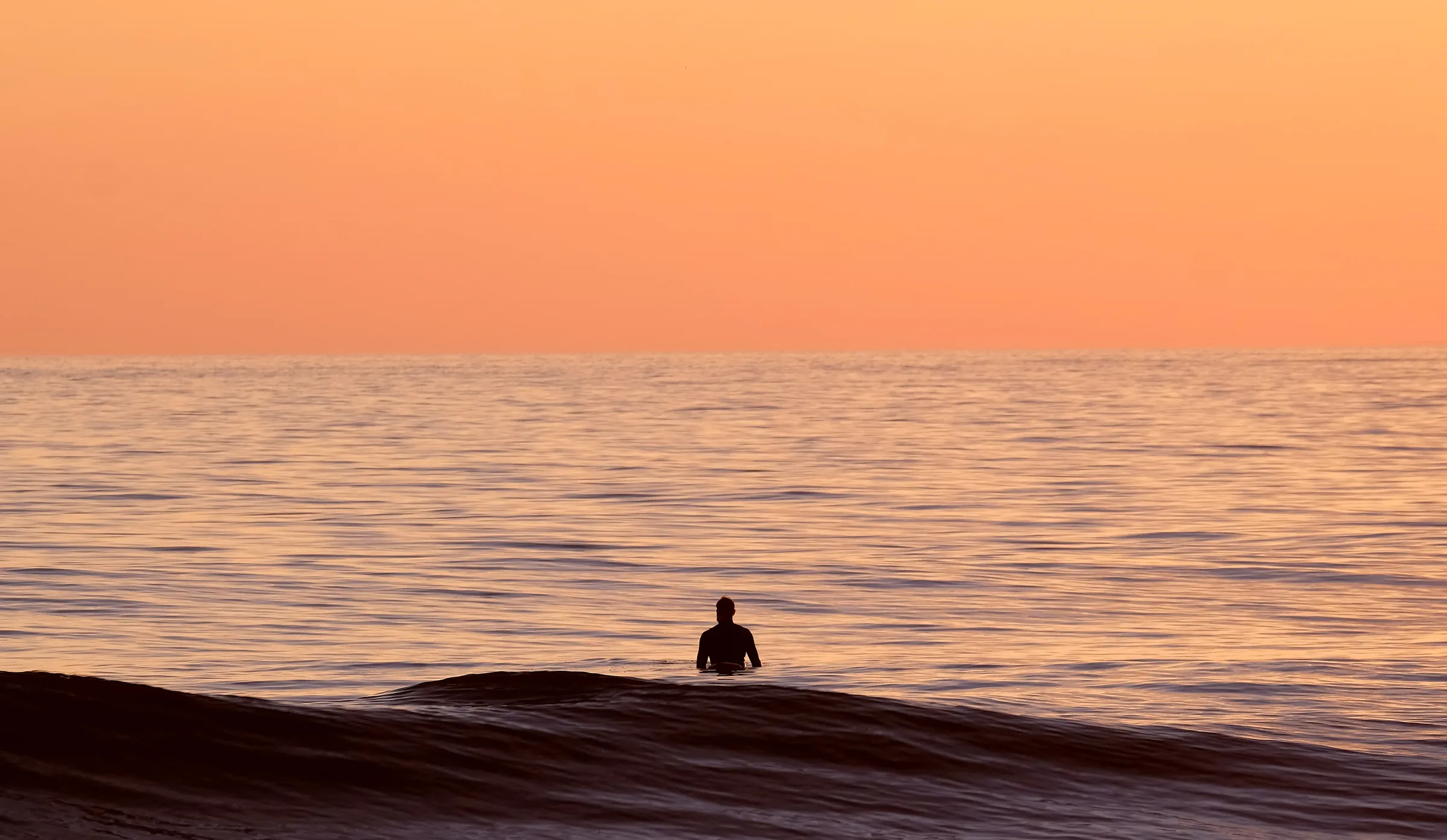 A surfer in the Pacific at sunset in Oceanside, California